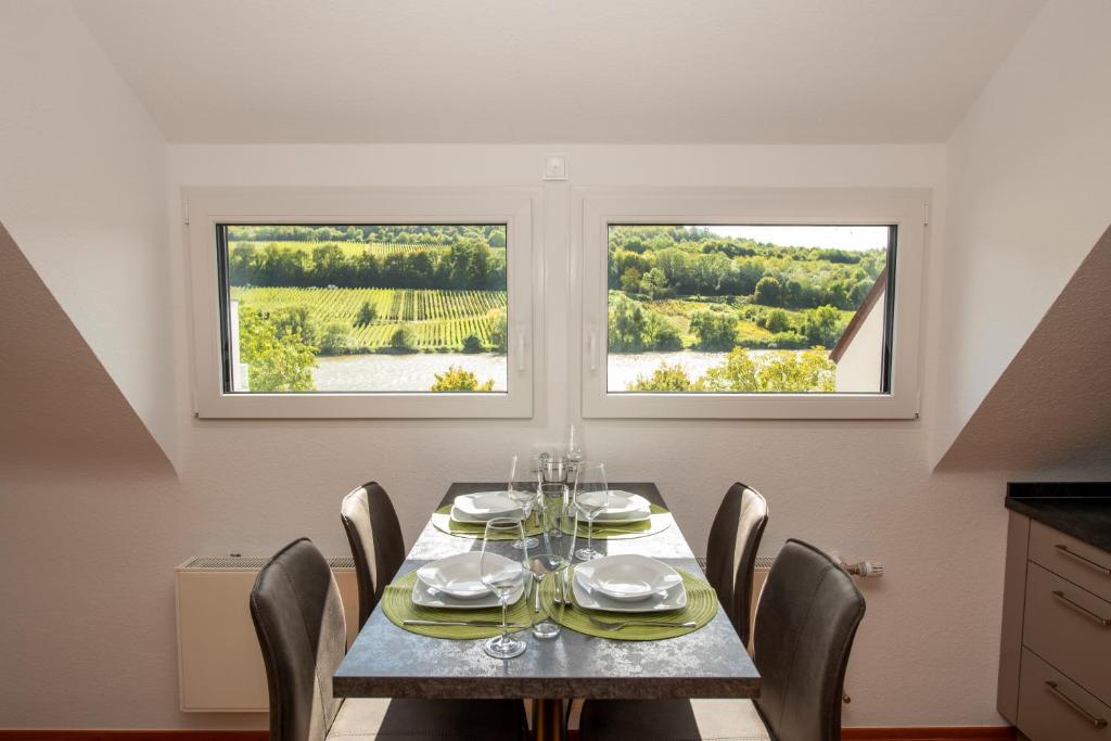 a dining room with a table and chairs and two windows at Ferienwohnung Moselblick Zell-Merl - Merllorca DG Panoramablick & Parkplatz in Zell an der Mosel
