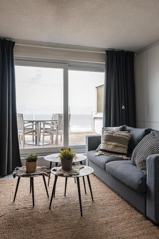 a living room with a couch and tables in front of a window at Seaview Penthouse with Terrace Nieuwpoort in Nieuwpoort