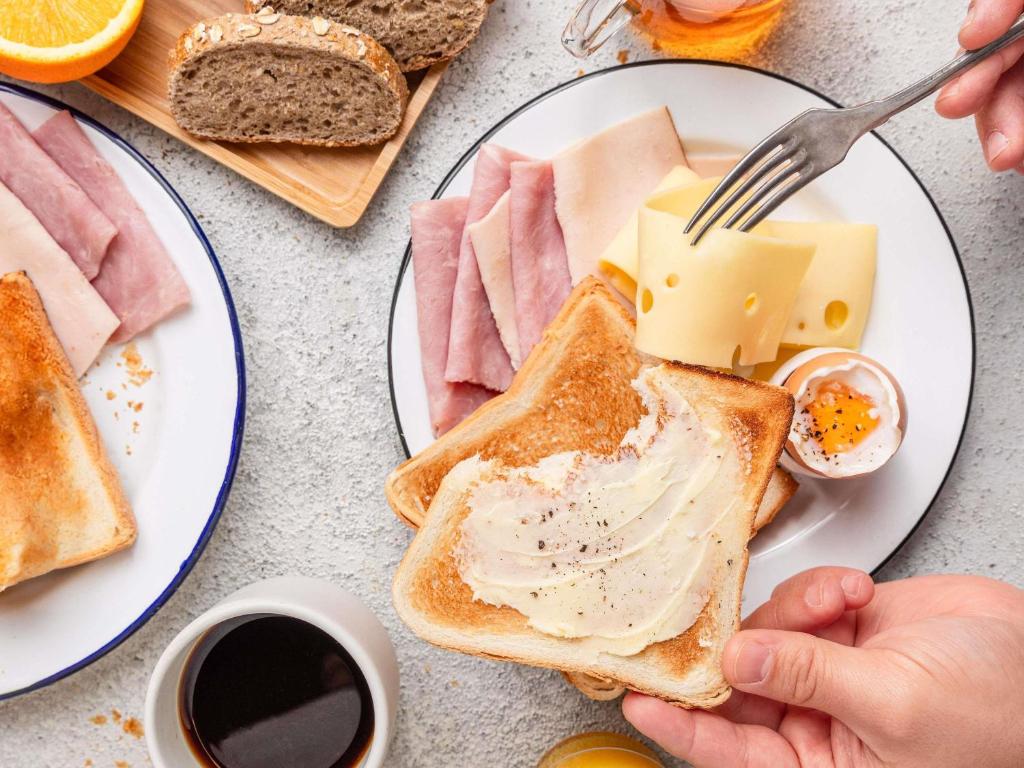 eine Person isst einen Teller Toast mit Butter und Käse in der Unterkunft Ibis Budget La Rochelle Puilboreau in Puilboreau