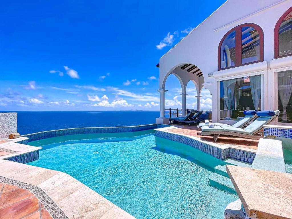 a swimming pool in front of a house with the ocean at Villa Leones Breathtaking Views and Authentic Charm in Oyster Pond
