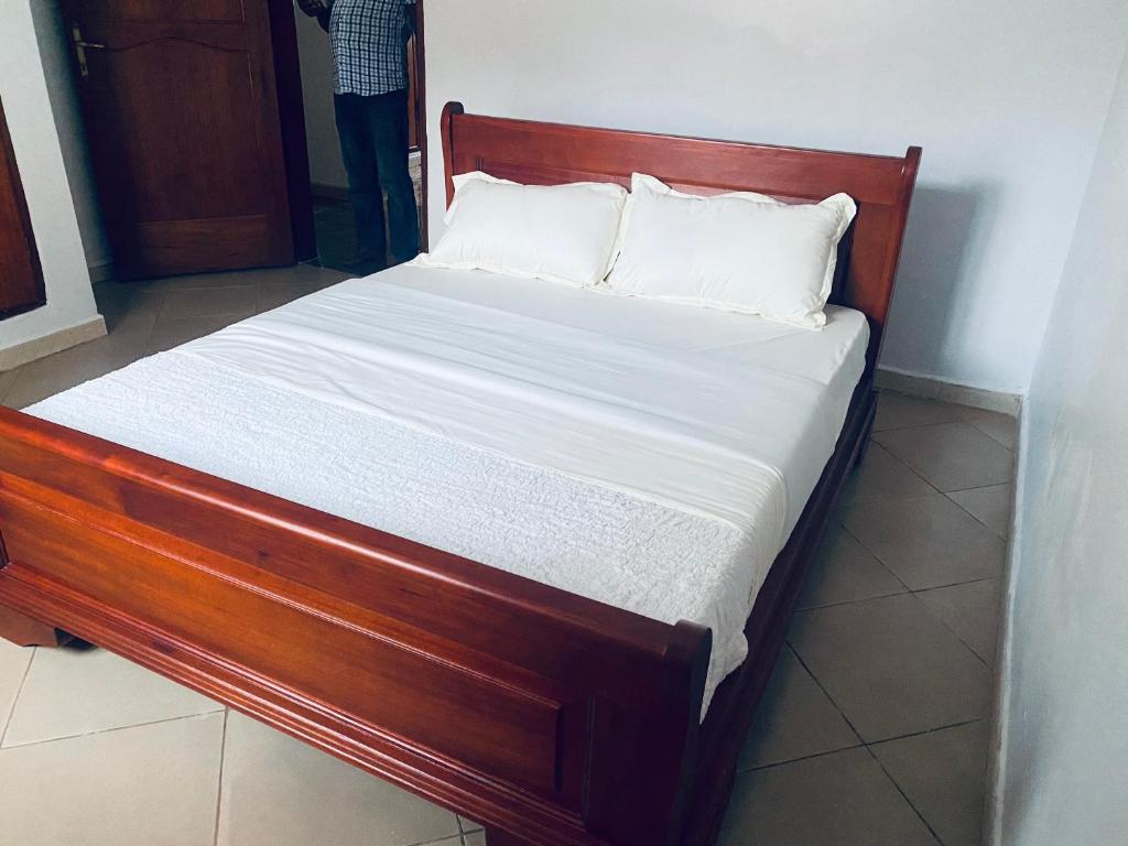 un letto in legno con lenzuola e cuscini bianchi di Paradise pathways lweza a Mutungo