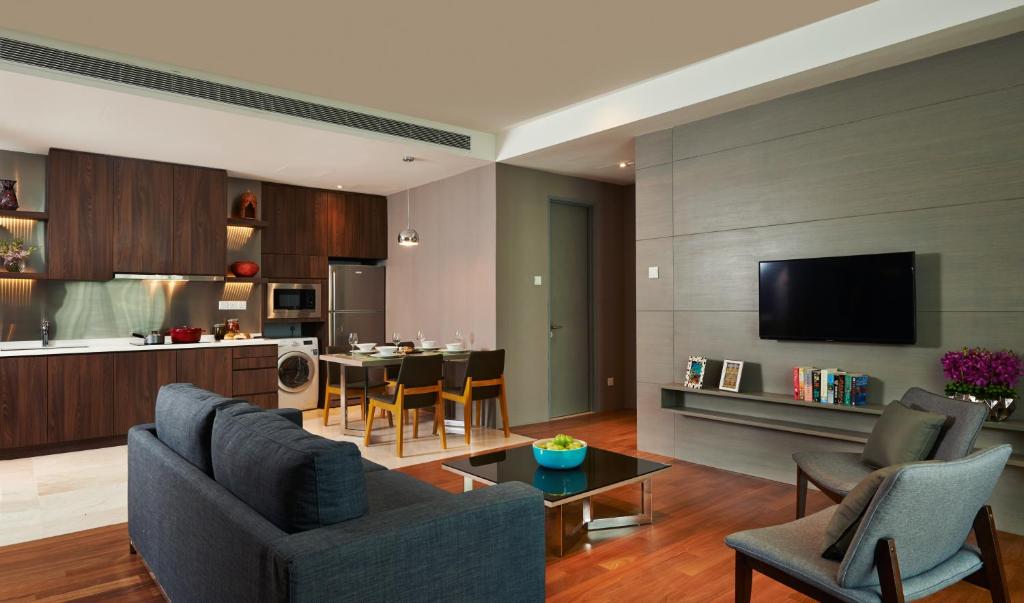 A serviced-apartment living room with a sofa, television, dining area and open kitchen.