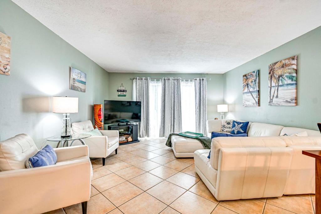 a living room with white couches and a tv at Steps to Sand Condo with Pool Access in Cocoa Beach in Cape Canaveral