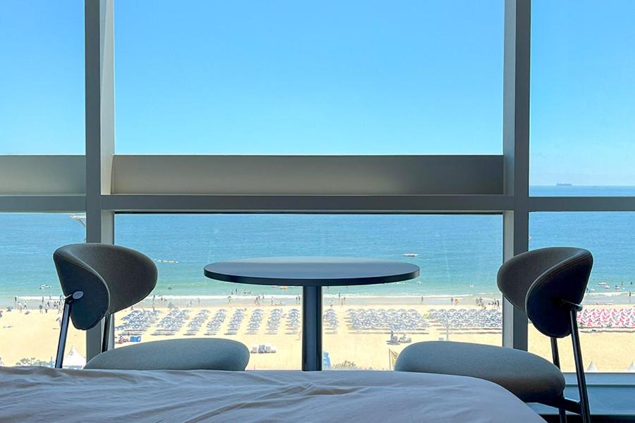 a bedroom with a view of a beach and a table and chairs at 코브스테이 해운대 in Busan