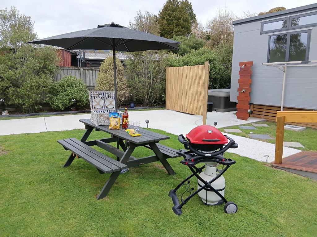 a picnic table with a grill and an umbrella at Tawa Tiny Stays Luxury adults only with spa in Taupo