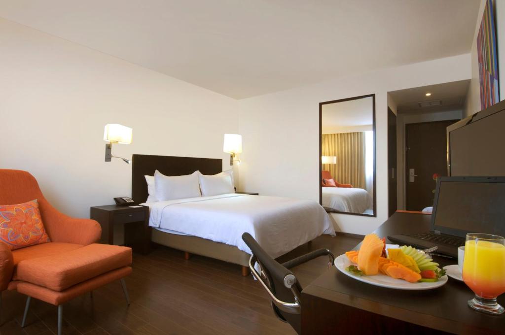 A polished guest room with a king bed, work desk, armchair, and in-room refreshments.