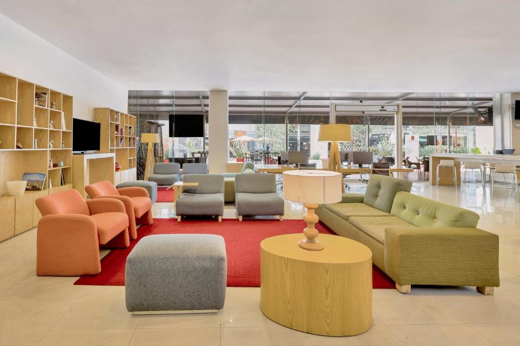 A bright hotel library lounge with sofas, armchairs, bookshelves, and a red rug.