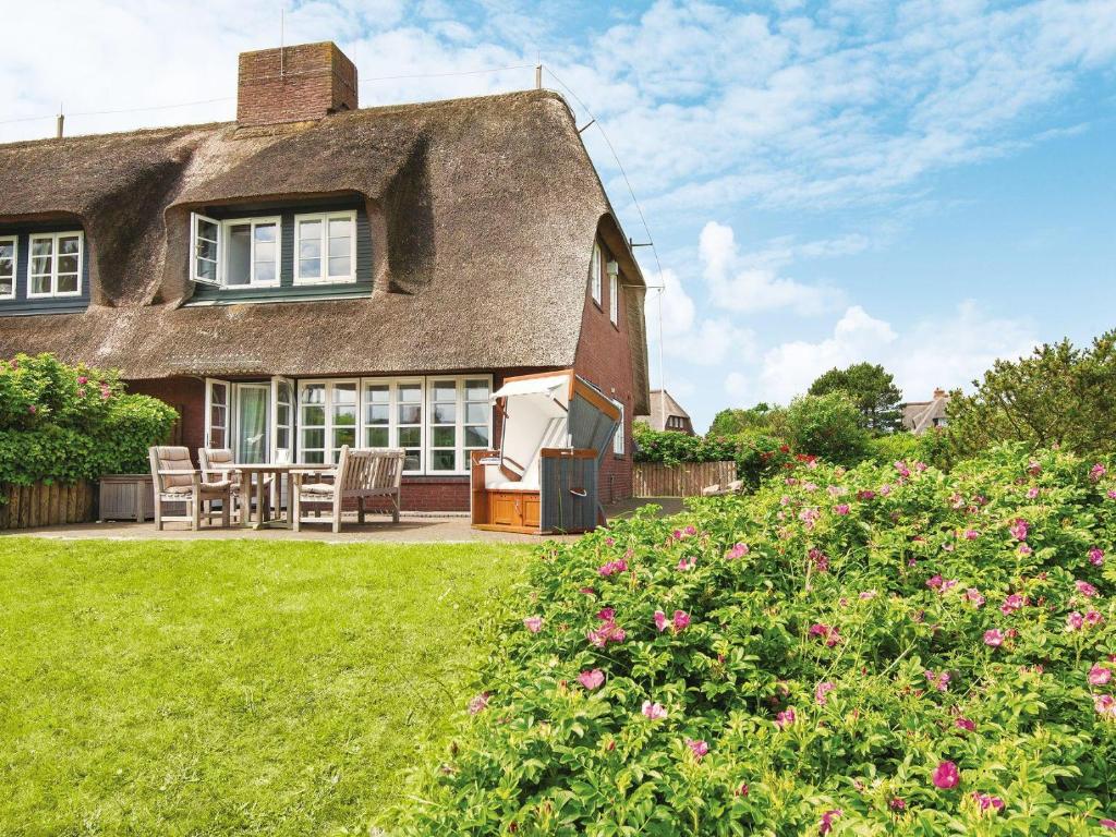 a thatch roofed house with a patio and flowers at Wattenhof-1 in Kampen