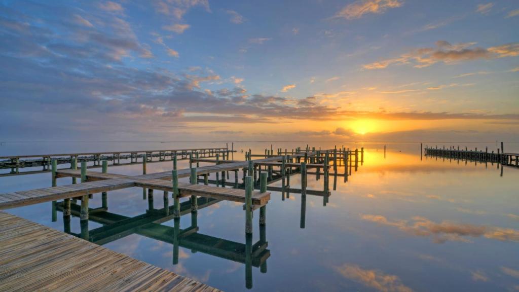 a pier on the water with the sunset in the background at 6BDR Bay Haven w Shared Waterfront Pool Boat Dock Keeper Trout by AvantStay in Padre Island