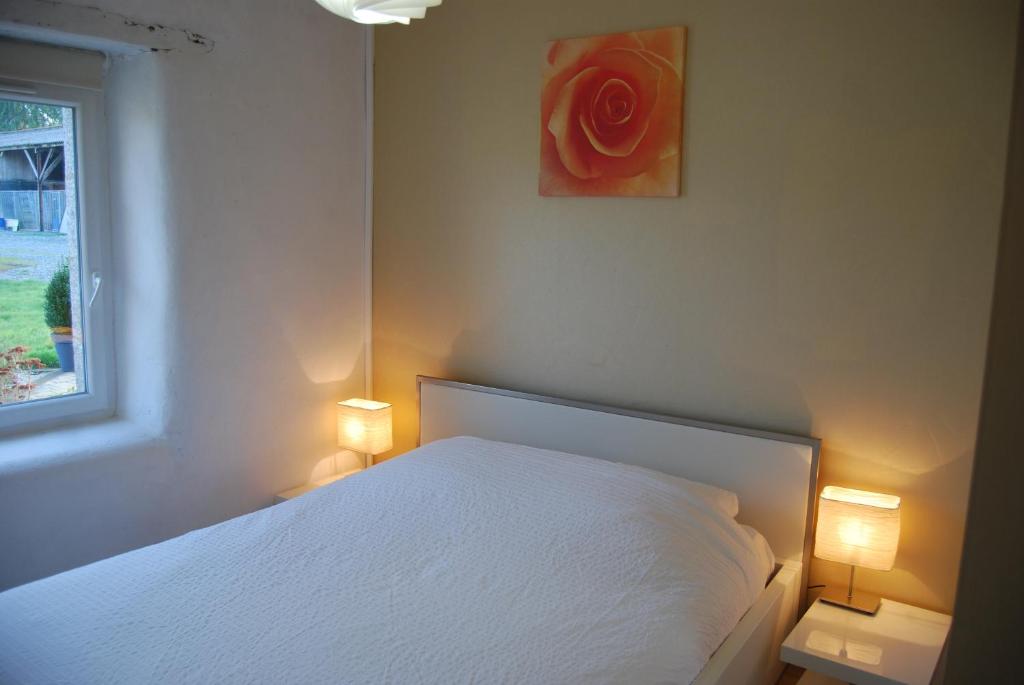 a bedroom with a white bed with two lamps and a red rose at Maison à la campagne in Louargat