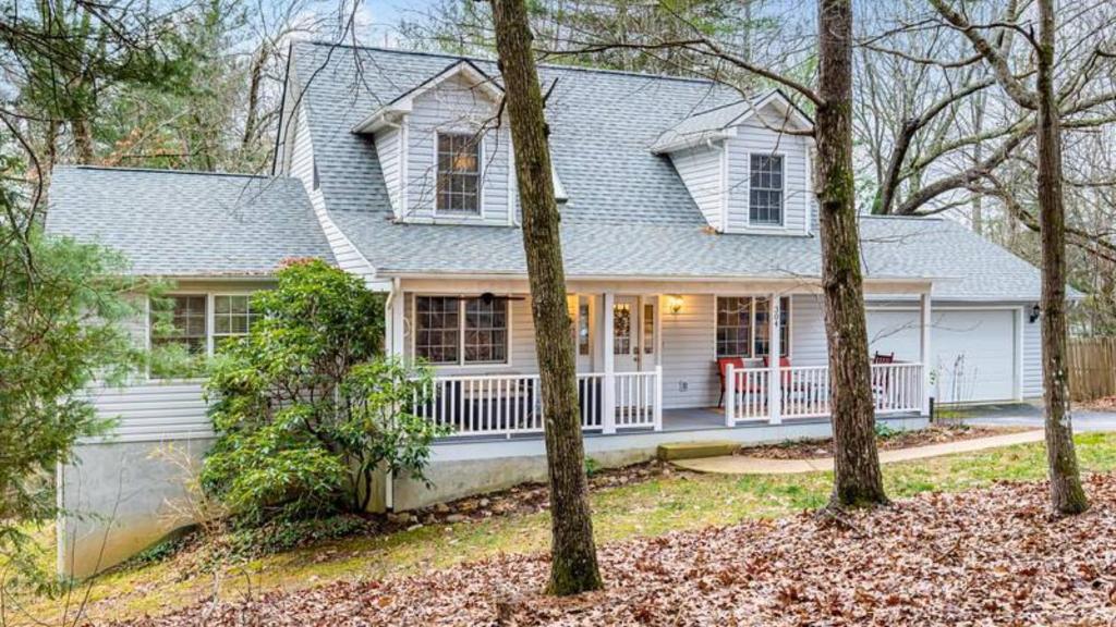 une maison blanche avec une véranda et des arbres dans l'établissement Asheville Cottage Retreat by AvantStay A Charm, à Fairview