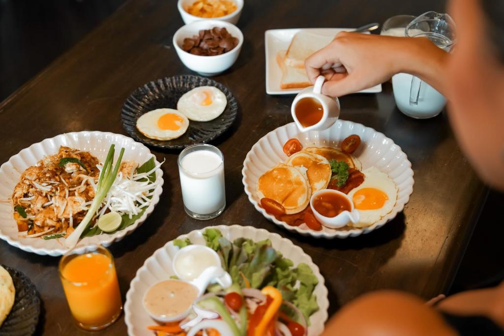 A breakfast table holds eggs, pancakes, rice, salad, fruit and drinks.