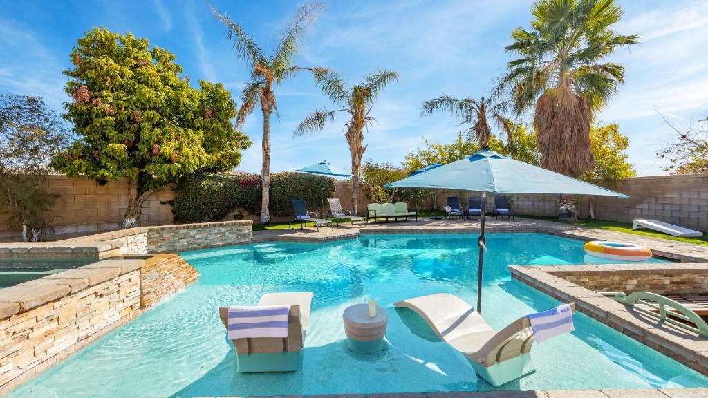 a swimming pool with chairs and an umbrella at Luxury Oasis w Pool Hot Tub Fire Pit Games Big Yard Larrea by AvantStay in La Quinta