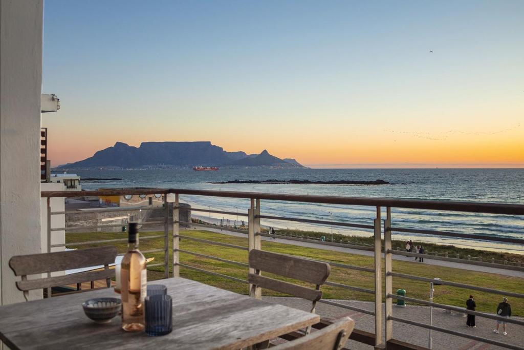 a bottle of wine on a table on a balcony overlooking the beach at Eden on The Bay 250 in Bloubergstrand