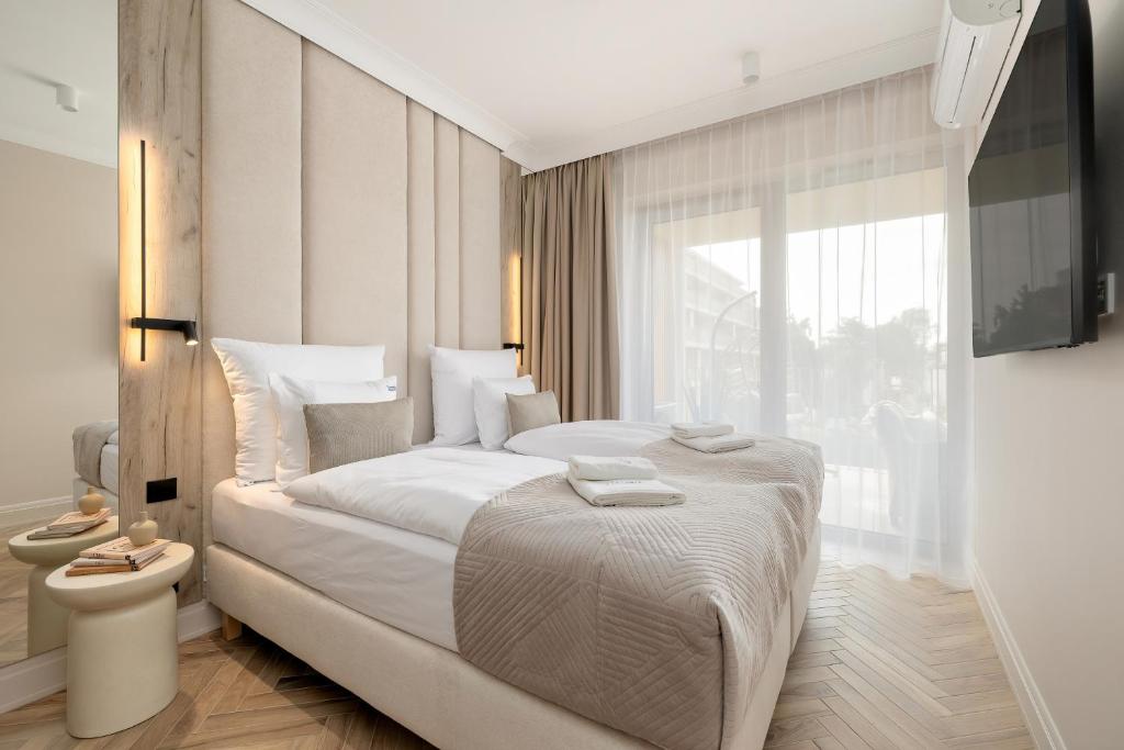 ein weißes Schlafzimmer mit einem großen Bett und einem Fenster in der Unterkunft GREENERI PARK - Ambria Apartments in Świnoujście