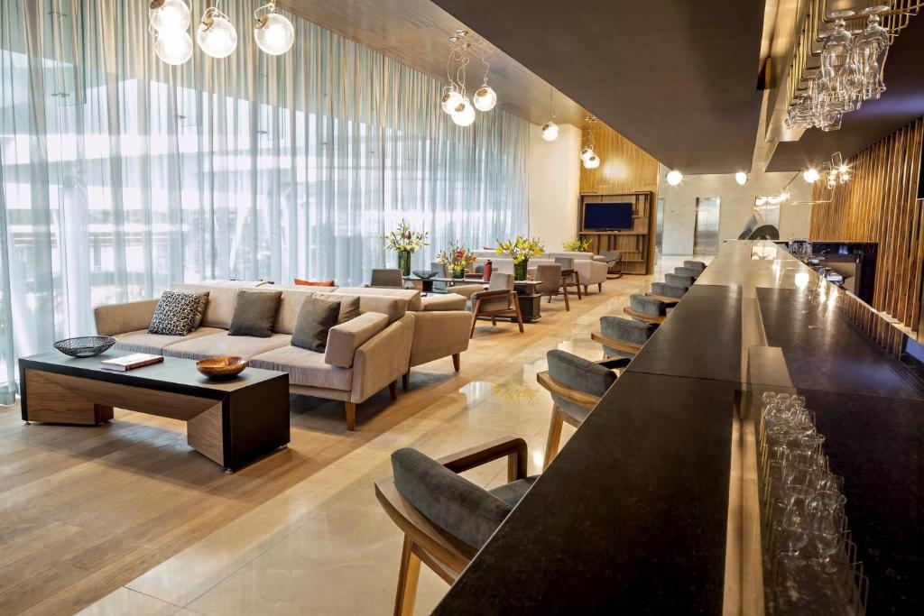 A long bar anchors a bright lounge filled with sofas, tables, and window light.