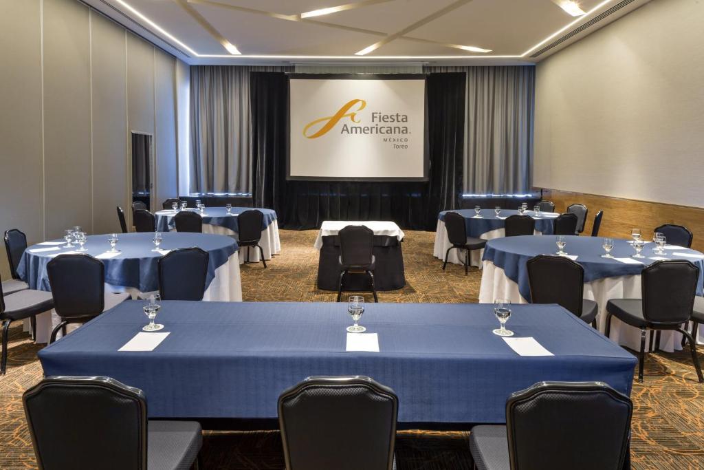 A presentation room with blue-clothed tables facing a branded projection screen.
