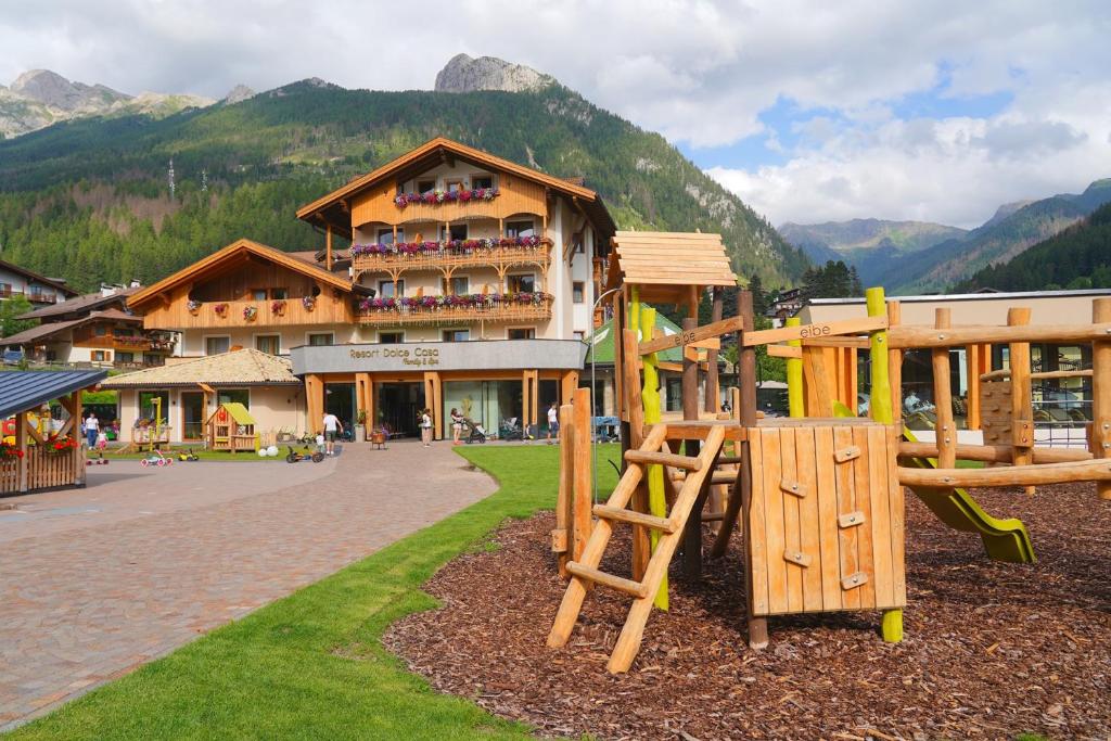 a playground in front of a building with a mountain at Resort Dolce Casa - Family & Spa Hotel in Moena