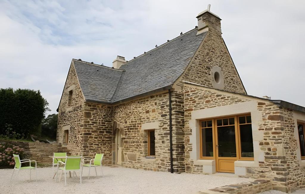 a stone building with green chairs and a table at Propriété De Campagne Typique in Brasparts