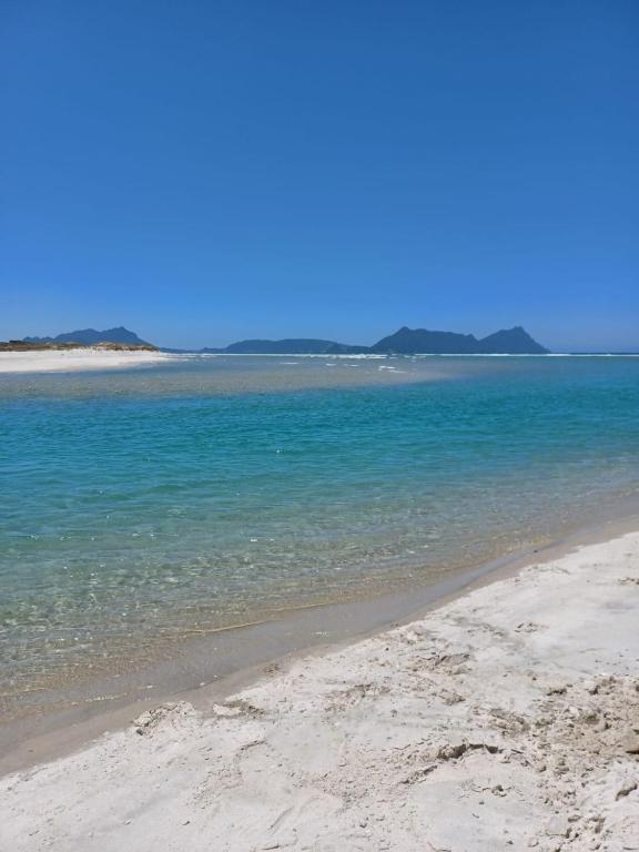 a sandy beach with blue water and mountains in the background at Cosy Cottage in Ruakaka