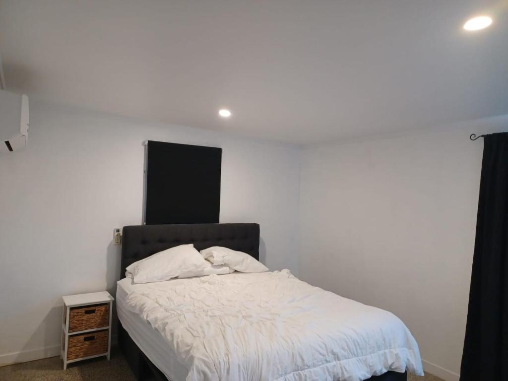 1 dormitorio con cama blanca y cabecero negro en Cosy Cottage, en Ruakaka