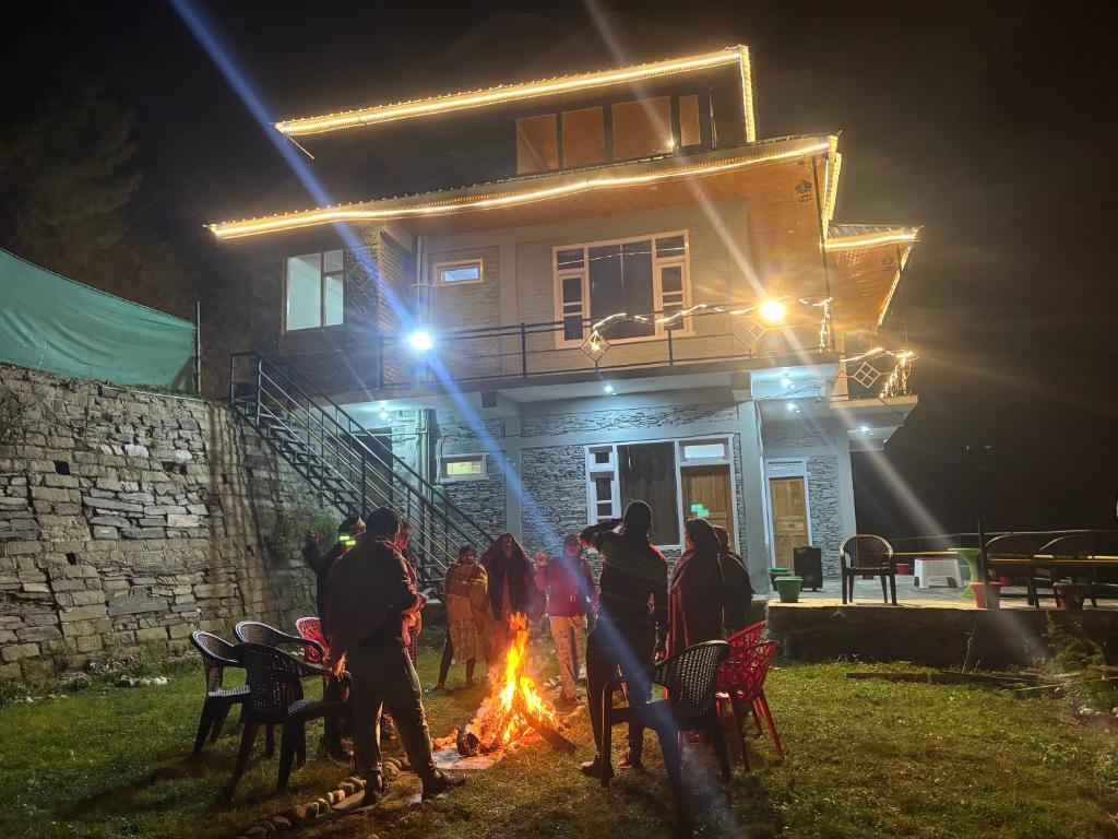 Eine Gruppe von Menschen steht um ein Feuer vor einem Haus in der Unterkunft River Era by Naavagat in Jibhi