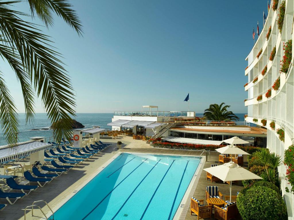 a swimming pool with chairs and the ocean in the background at Gran Hotel Reymar in Tossa de Mar