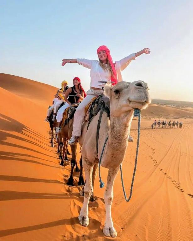 a group of people riding on a camel in the desert at Merzouga Desert Tents in Merzouga