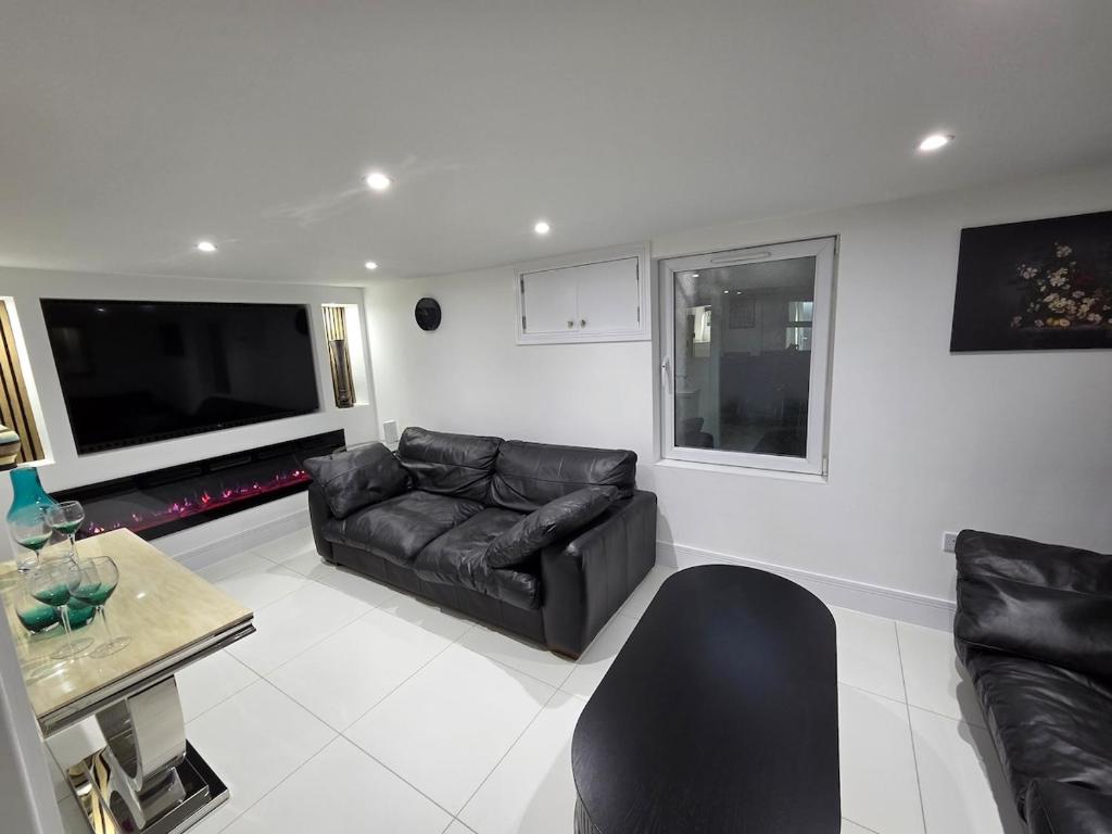 a living room with a black leather couch and a tv at Stylish 6-Bedroom House, Town Centre, Sleeps 14, With Garden in Merthyr Tydfil