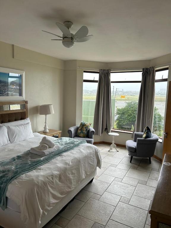 a bedroom with a bed and two chairs and windows at Daisy Accommodation & Spa in Cape Town