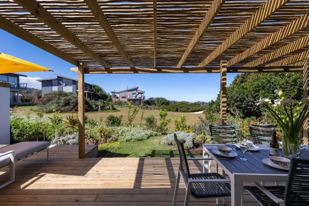 eine Terrasse mit einem Tisch und Stühlen unter einer hölzernen Pergola in der Unterkunft Oyster Cottage in Plettenberg Bay