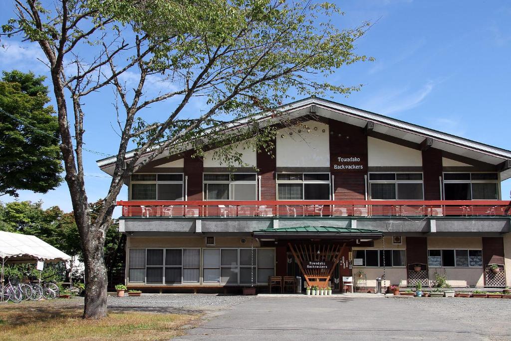 a large building with a balcony and a tree at Towadako Backpackers in Towada