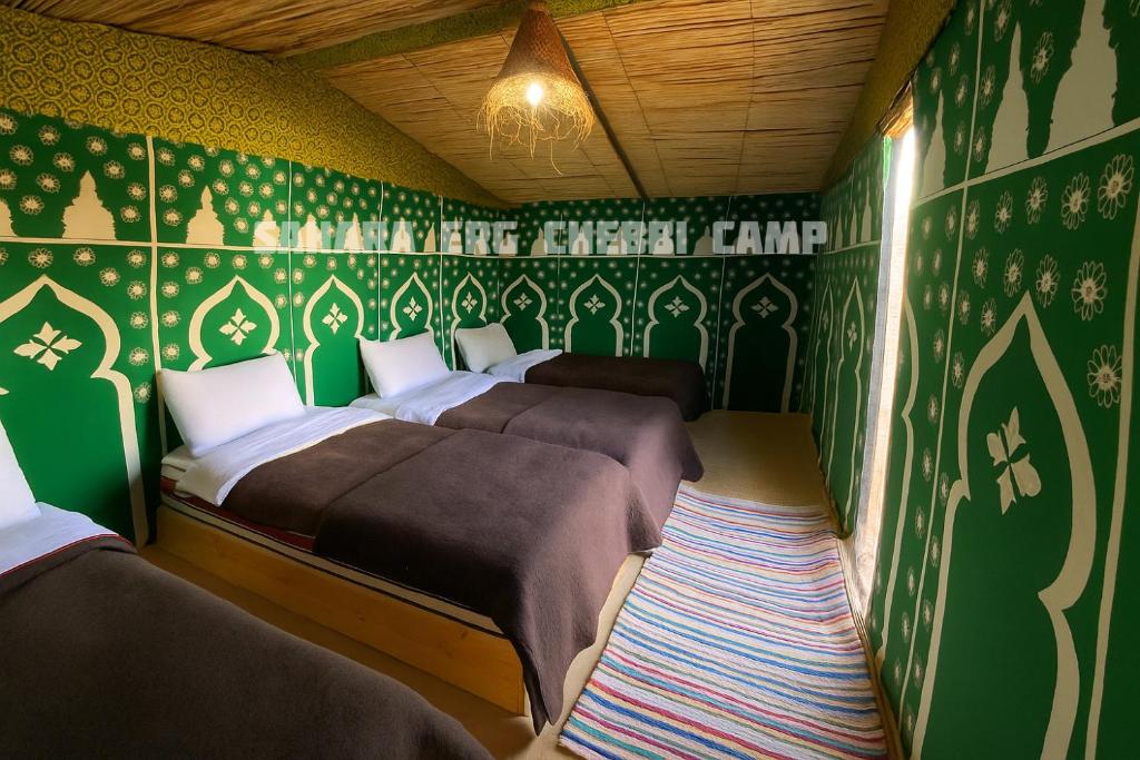 Tres camas en una habitación con papel pintado verde y blanco. en Sahara Erg Chebbi Camp, en Merzouga
