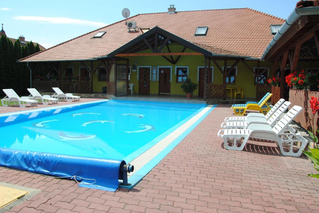 a swimming pool with white chairs and a house at NAPSUGAR VENDÉGHÁZ in Bogács