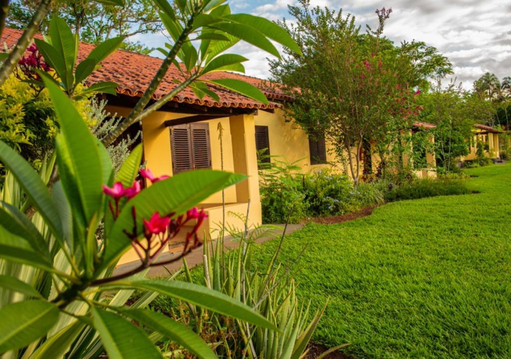 a yellow house with a green yard with pink flowers at Hotel Fazenda Bela Vista in Dourado