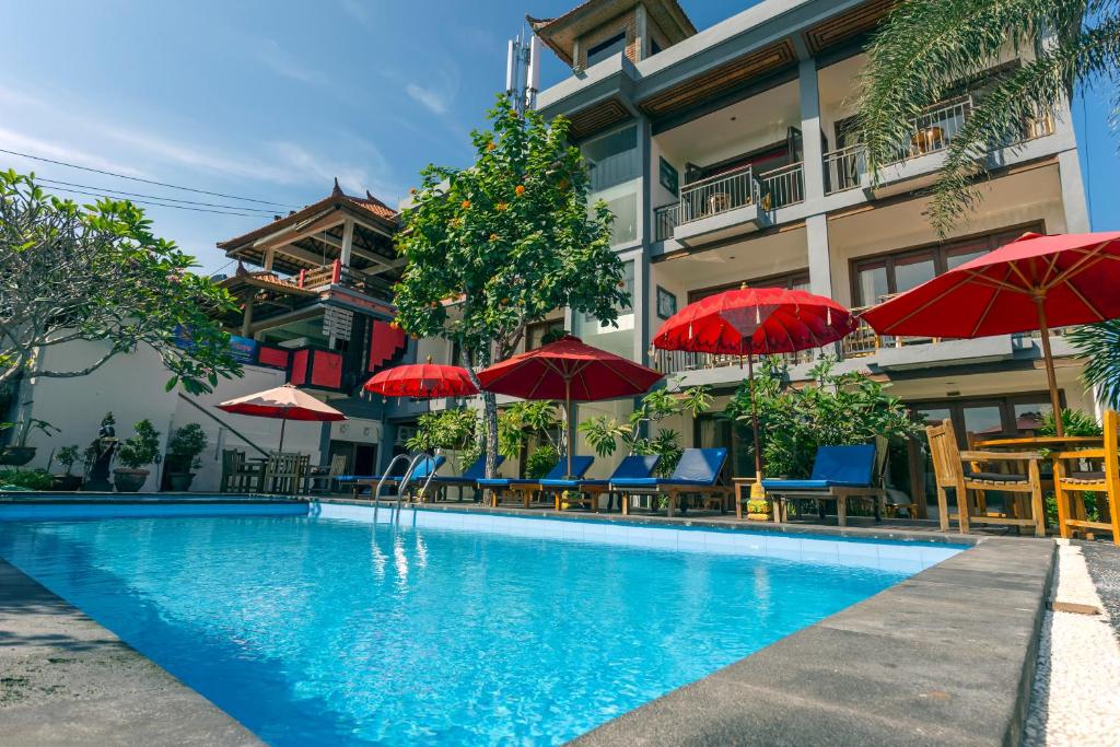 a swimming pool with umbrellas and chairs and a building at Waroeng Surya Home Stay in Uluwatu