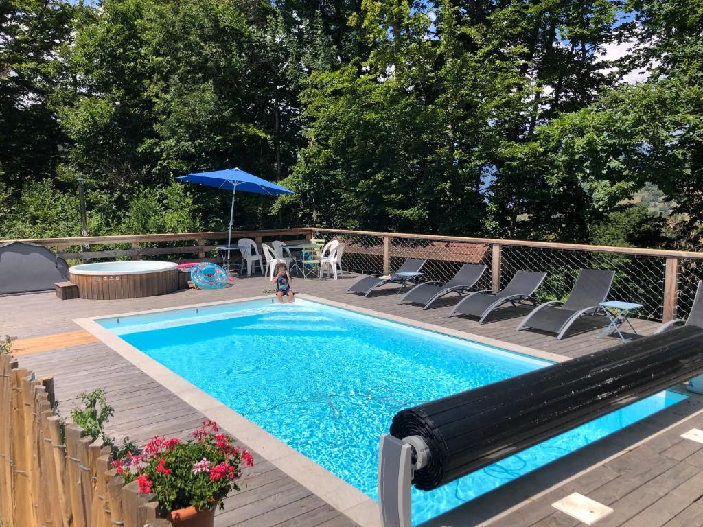 a swimming pool on a deck with chairs and an umbrella at Gîtes du Grand Replomb, Les Artistes, Piscine et Jacuzzi in Sainte-Agnès