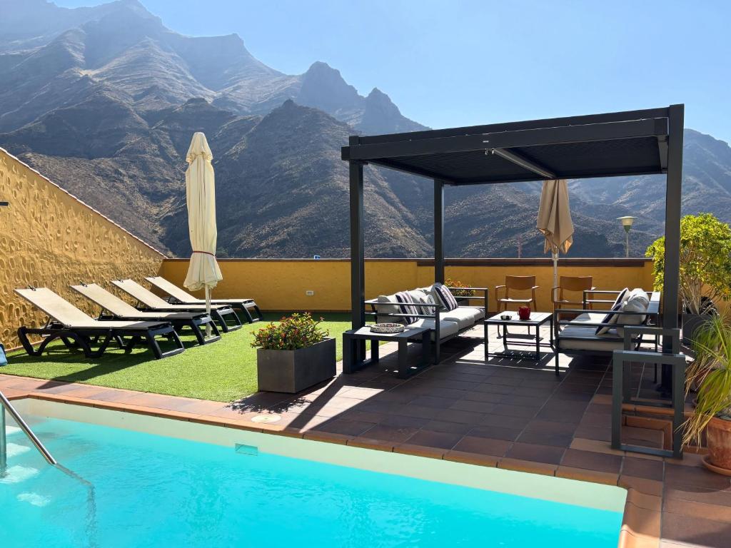 a pool with chairs and umbrellas next to a mountain at Los Veroles in Agaete