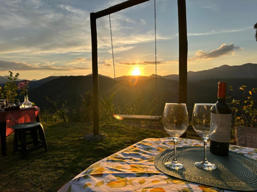 un tavolo con due bicchieri di vino e il tramonto di Village dos Alpes - Chalés na Montanha Teresópolis a Teresópolis