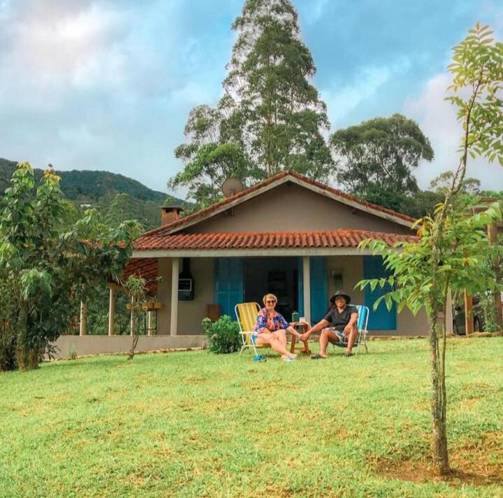 dos personas sentadas en sillas de jardín frente a una casa en Cantinho Paraíso da Mantiqueira SFX pet friendly, en São Francisco Xavier