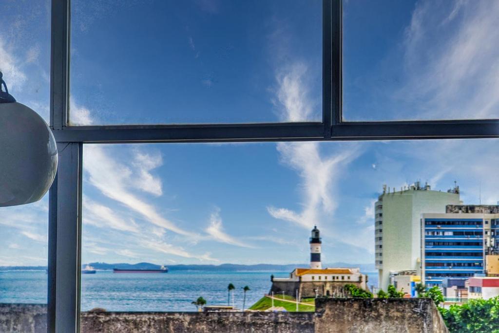 a view of the ocean and a lighthouse from a window at Apartamentos na BARRA com VISTA MAR, a 1 minuto da praia e do Circuito do Carnaval - SEAVIEW PRIVATE APARTMENTS in Salvador
