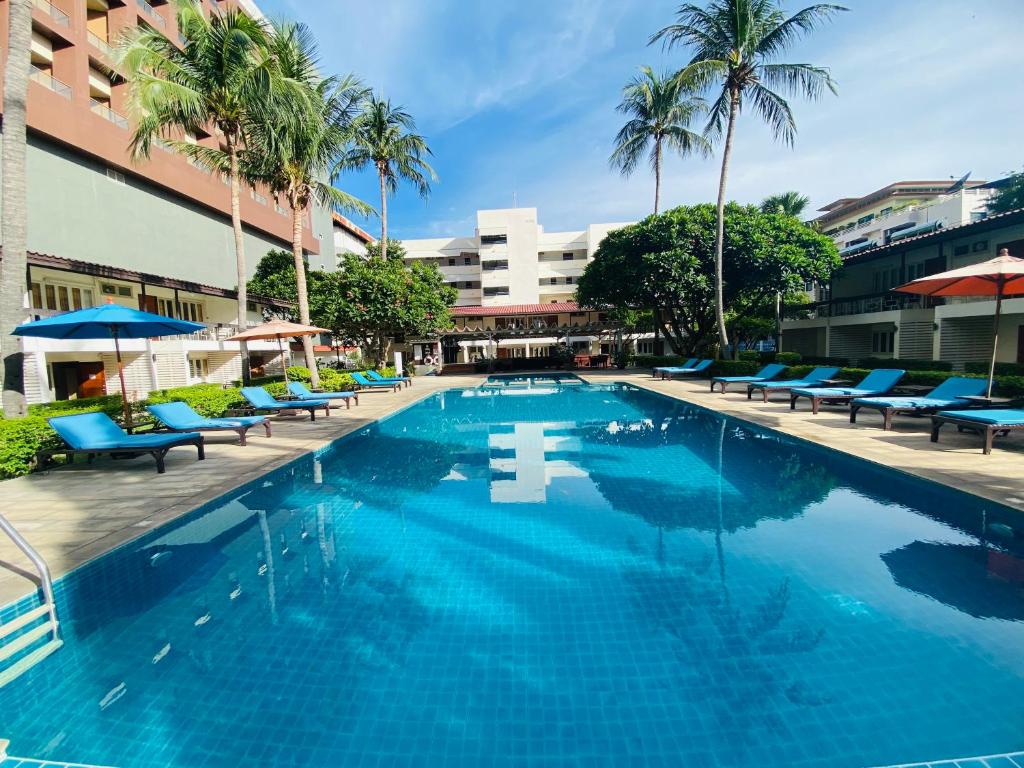 a large swimming pool with blue chairs and palm trees at Nautical Inn in Pattaya Central