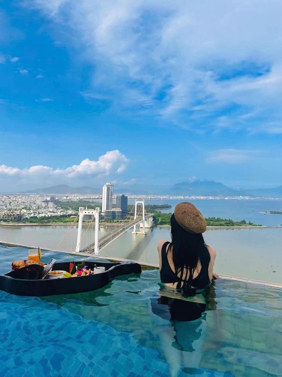 a woman sitting in a infinity pool with a boat in the water at Gold Apartment With Sea View In Da Nang Bay in Da Nang