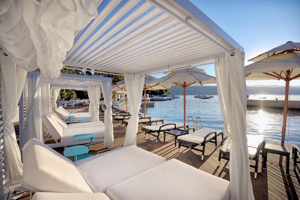 a porch with white chairs and umbrellas and the water at Amadria Park Grand Hotel 4 Opatijska Cvijeta in Opatija