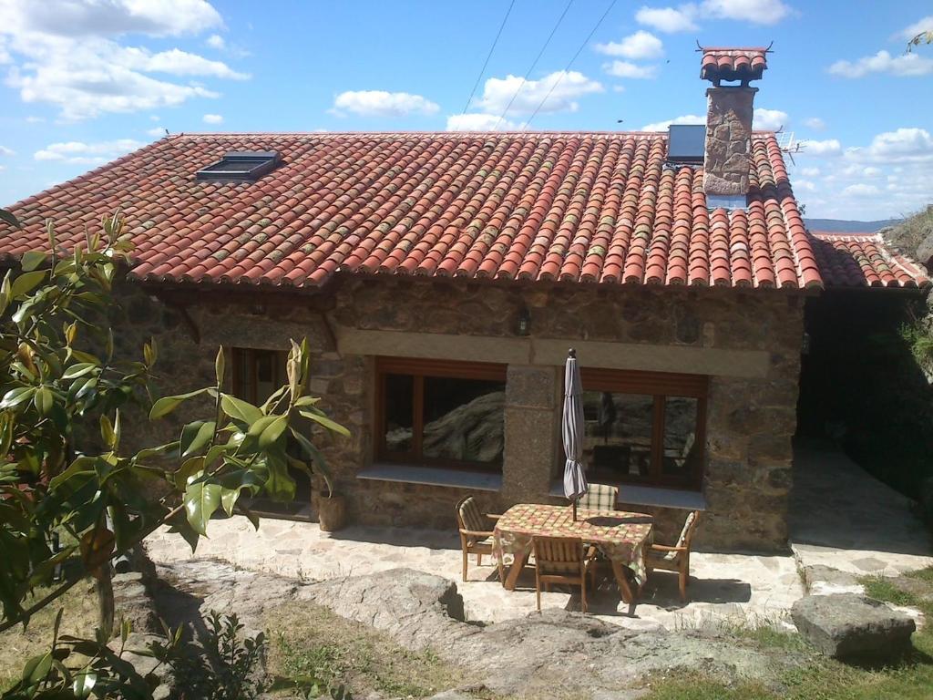 une petite maison en pierre avec une table et un parasol dans l'établissement Molino de las Pontezuelas, à Piedrahíta