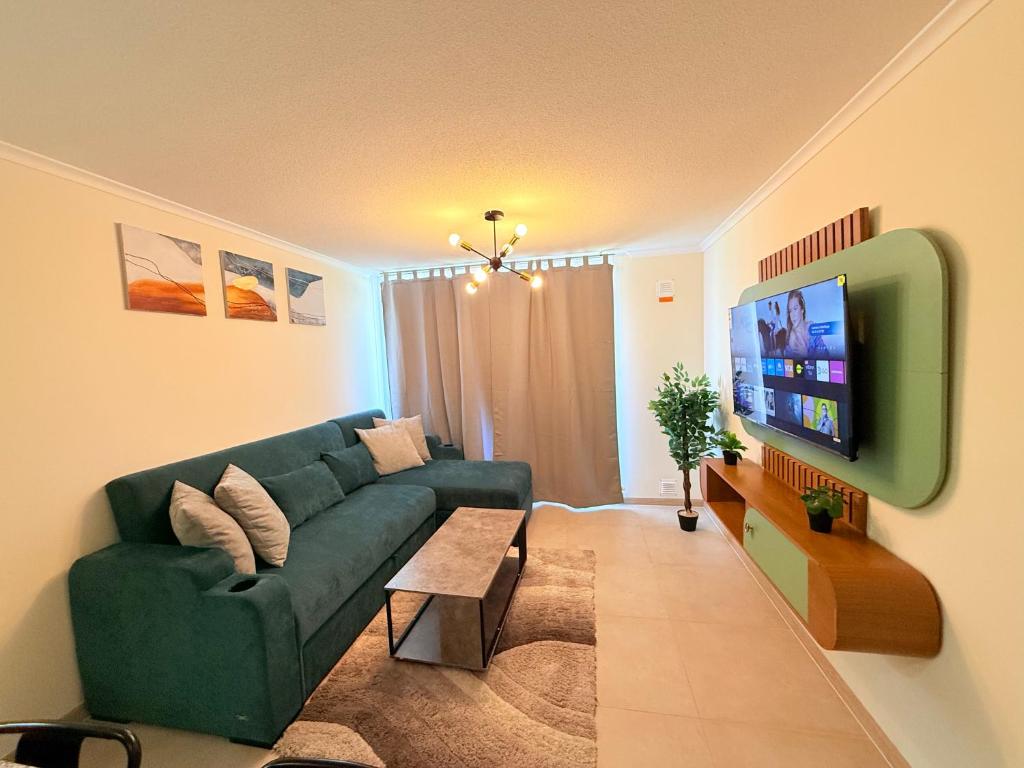 a living room with a green couch and a tv at Departamento con piscina a pasos de la playa en La Serena in La Serena