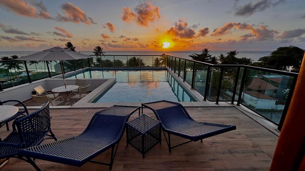 Un balcón con sillas y una piscina con la puesta de sol. en Design & Conforto Praia aos seus Pés Flats Mauê, en Tamandaré