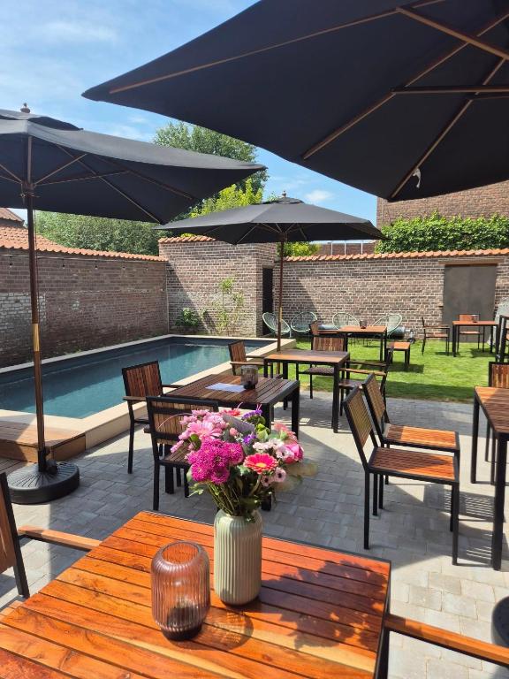 a patio with tables and umbrellas and a pool at Oud Tolkantoor in Alveringem