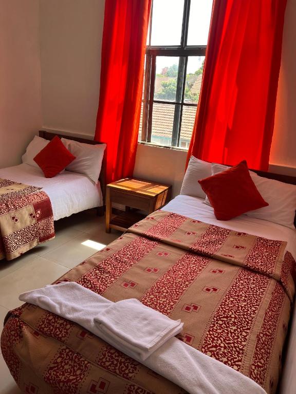 two beds in a room with red curtains and a window at Sadili Oval B & B in Nairobi
