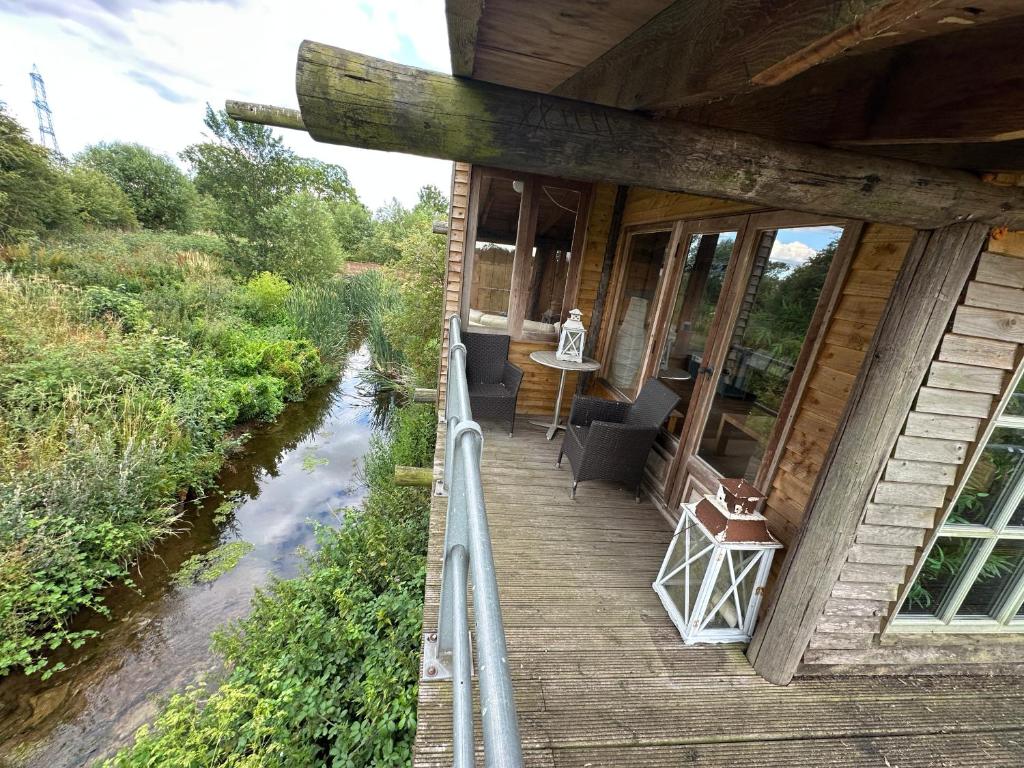 un portico di legno di una casa con un fiume di 5 Star Country Retreat, huge Log Cabin over small river, with private hot tub & log burner, WiFi, 65 inch smart TV relax read at Weston Newark, Nottinghamshire a Weston